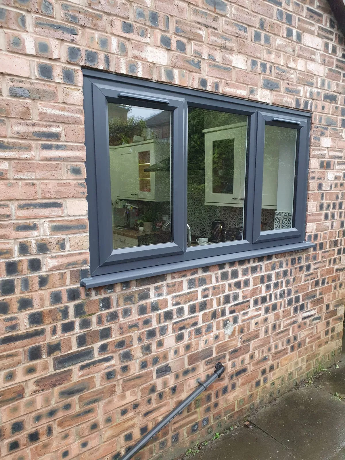 Anthracite grey three-pane casement kitchen window on a brick-built home