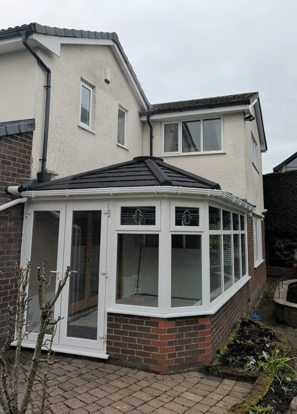 Victorian-style white PVC conservatory with dark tiled roof on a detached home