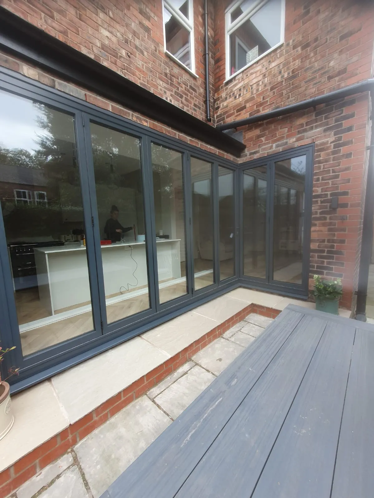 Anthracite grey aluminium bifold doors opening onto decking at a brick home