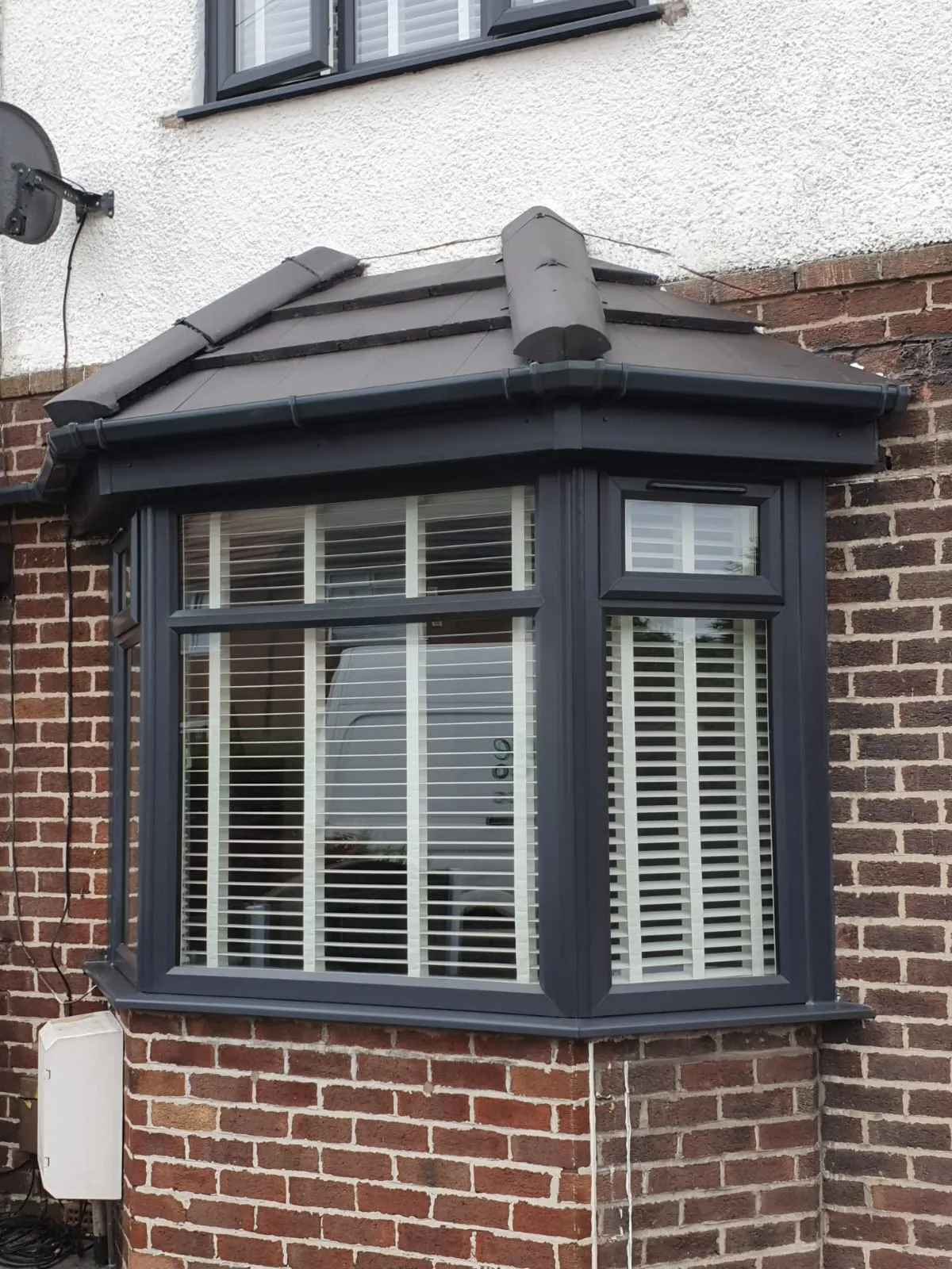 Anthracite grey bay window with tiled canopy on a red brick terrace in Manchester